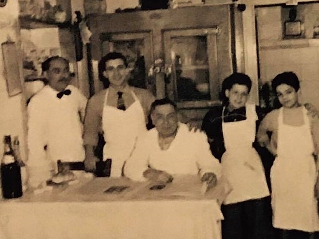 Il fondatore e il personale della trattoria dietro il banco, in una fotografia d'epoca color seppia